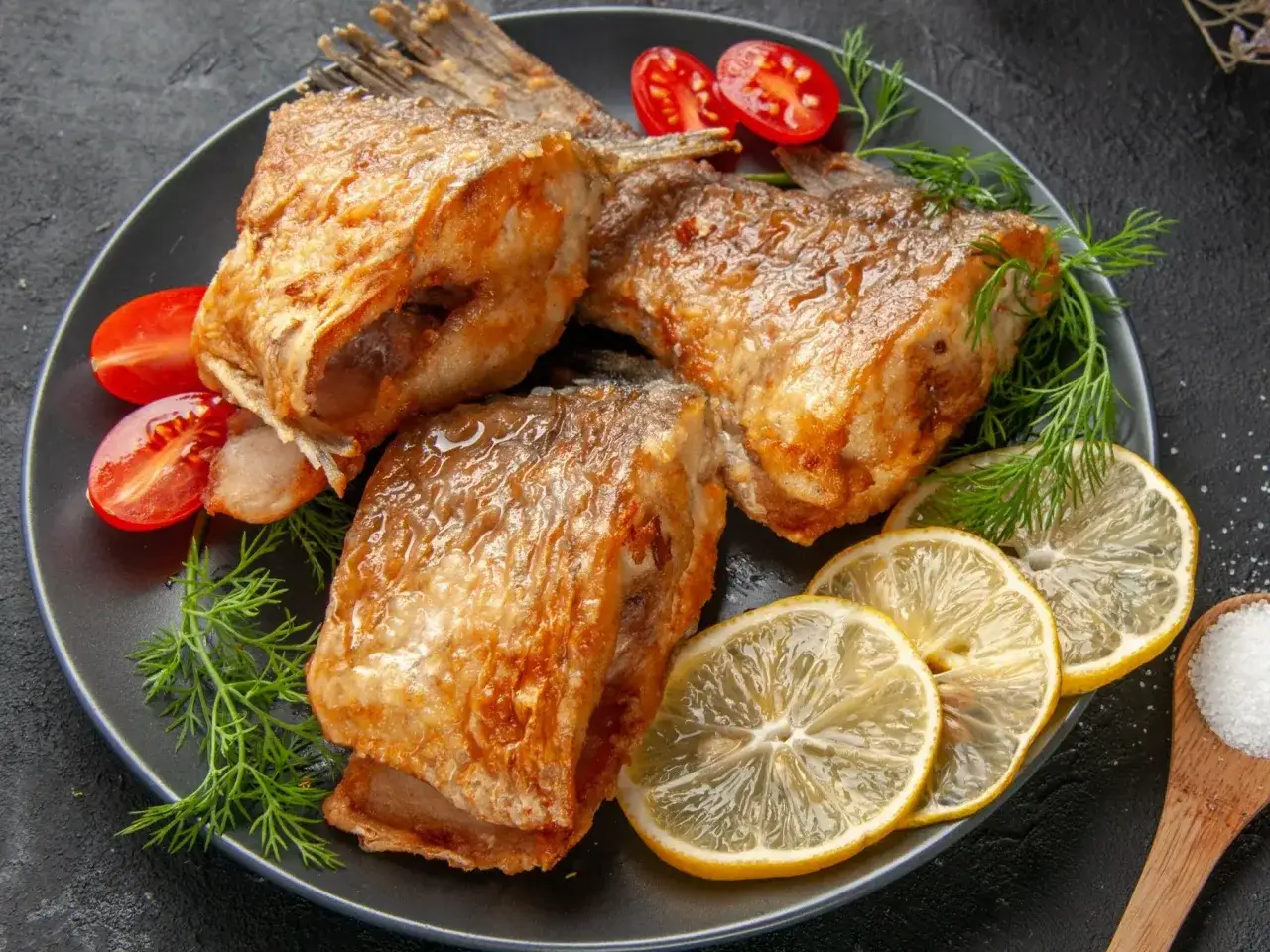 Smażony karp na talerzu z pomidorkami, cytryną i koperkiem. Czy karp jest zdrowy? Tak, to ryba bogata w białko i kwasy omega-3.