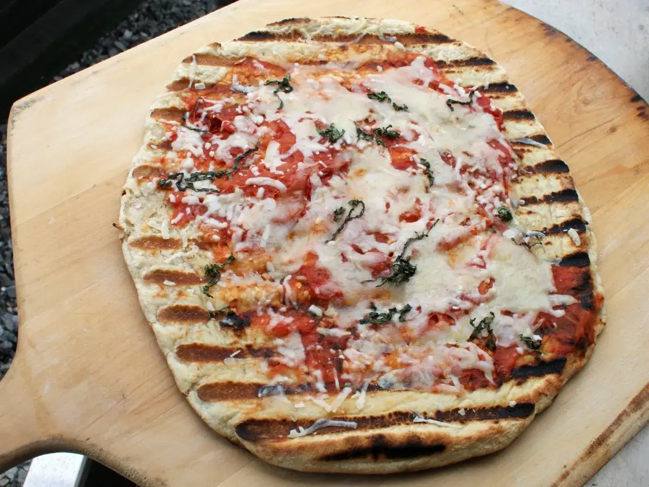 Pyszna pizza z grilla z ciągnącym serem i świeżą bazylią, podana na drewnianej łopacie.