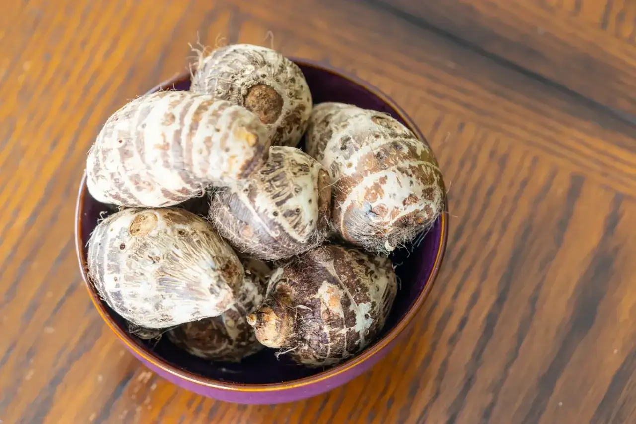 Kilka bulw taro w fioletowej misce na drewnianym stole.