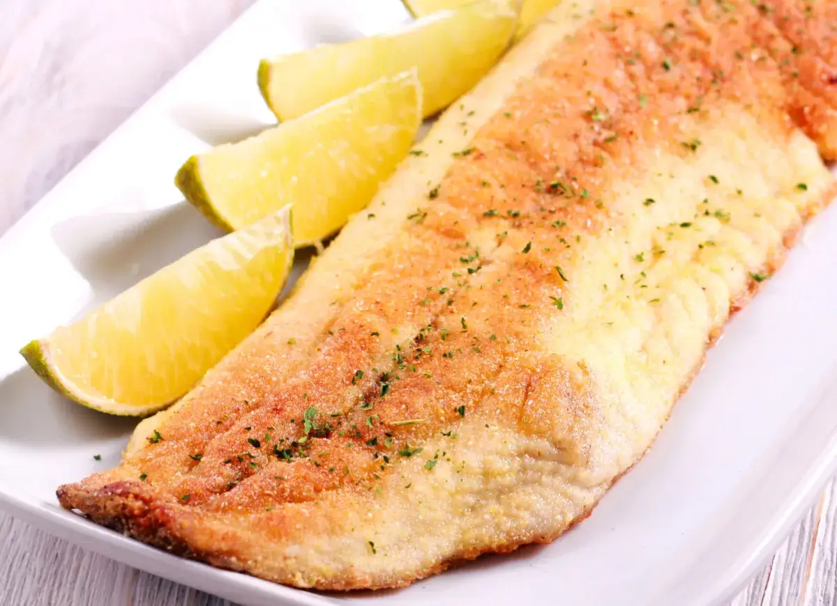 Smażony filet z ryby, podany z ćwiartkami cytryny. Czy amur ma dużo ości? Ten filet wygląda na pozbawiony ości, idealny do szybkiego posiłku.