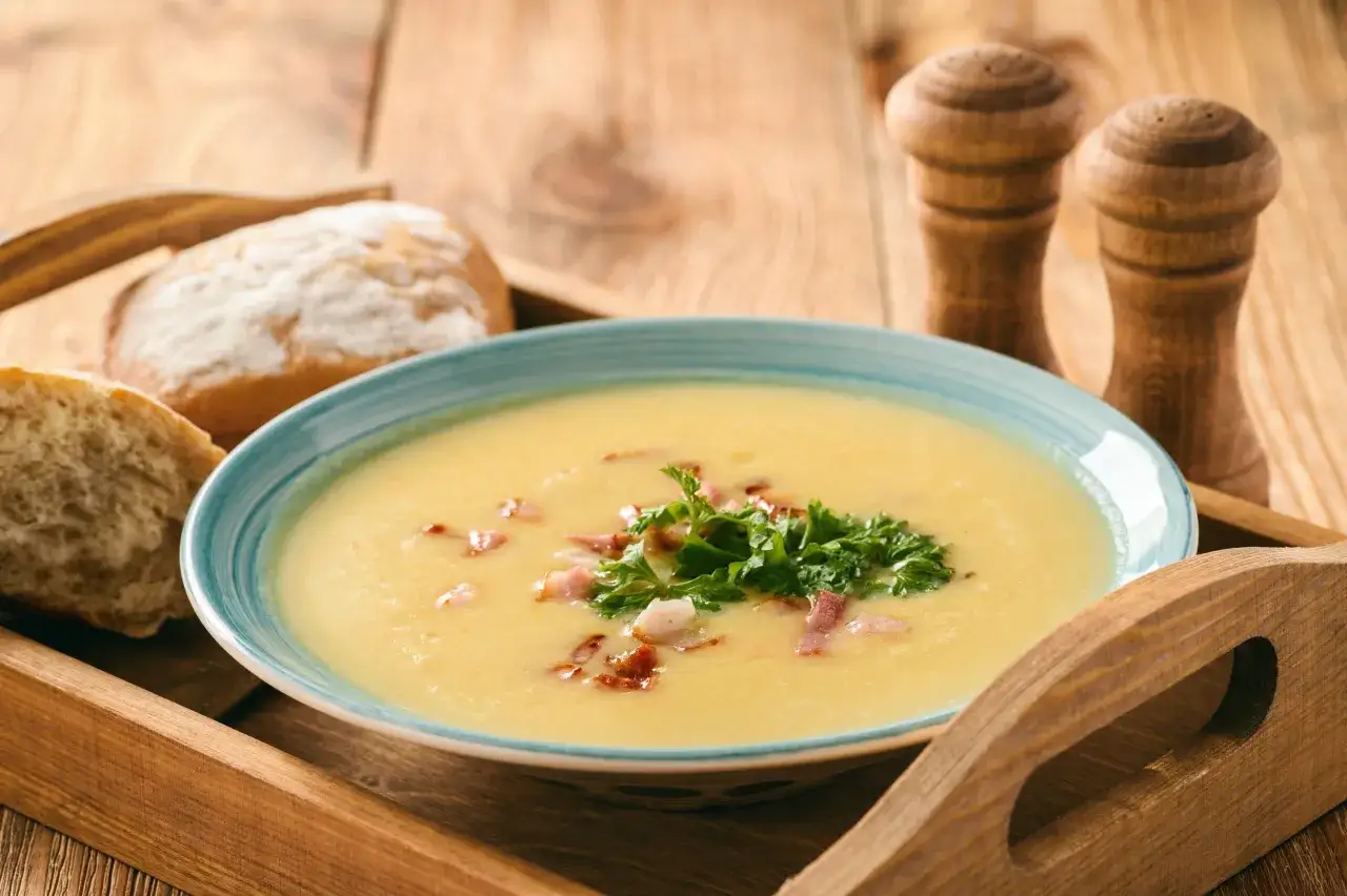 Aksamitna zupa krem z kiszonej kapusty, udekorowana boczkiem i natką pietruszki, podana z chrupiącym pieczywem.