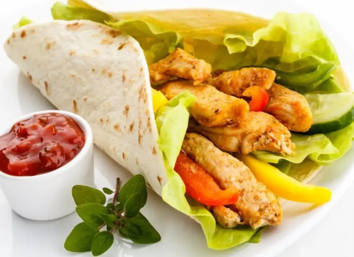 Pyszny kebab w tortilli z soczystym kurczakiem, chrupiącą sałatą, papryką i ogórkiem. Idealne kebab składniki na szybki posiłek.