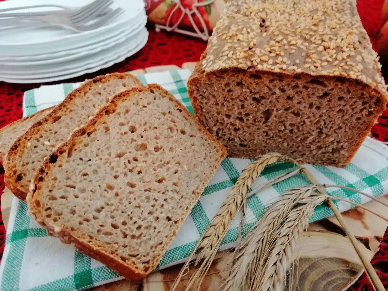 Chleb pełnoziarnisty z sezamem, pokrojony w kromki, wygląda jak najzdrowszy chleb. Obok kłosy zbóż.