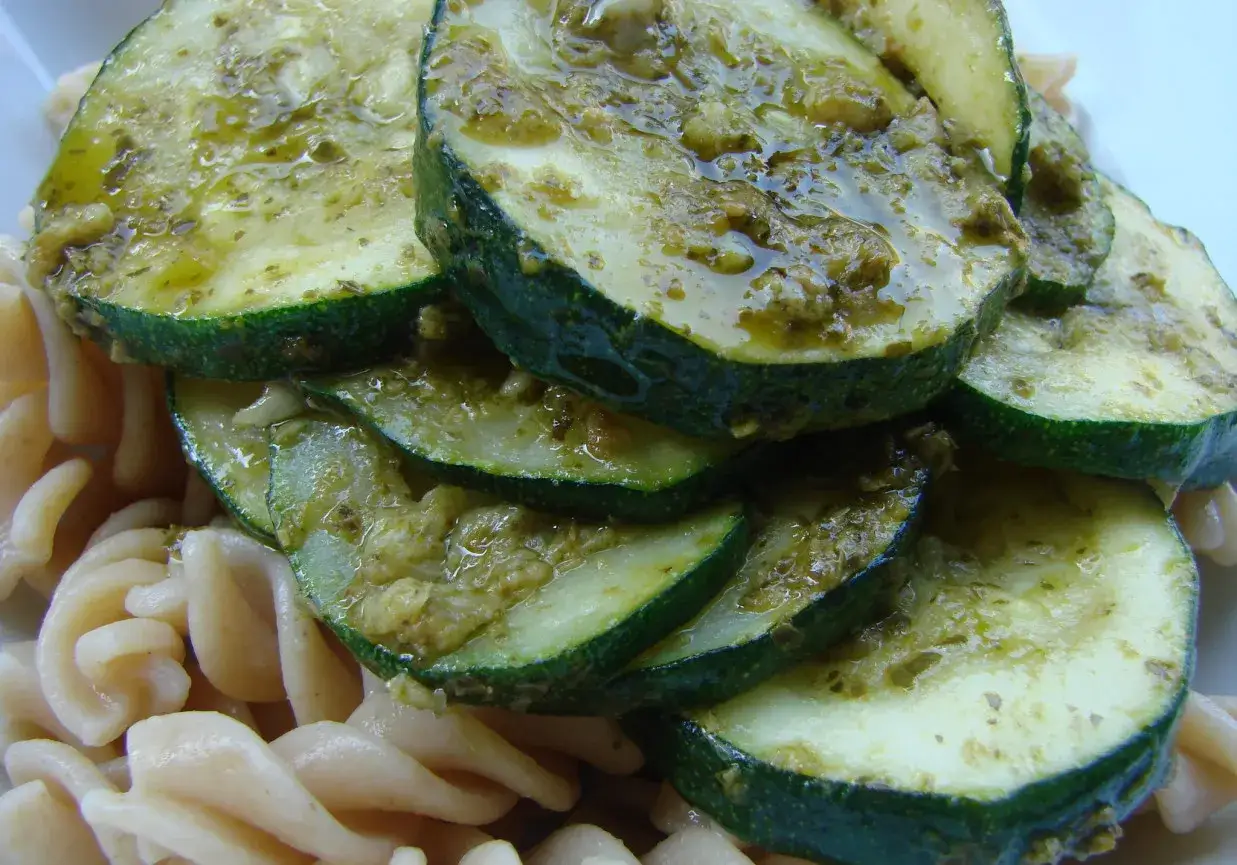 Smażona cukinia do obiadu, polana sosem pesto, leży na makaronie fusilli.