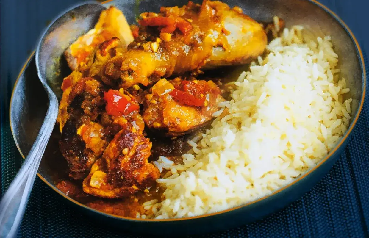 Pyszne mauritius jedzenie: kurczak w sosie z ryżem. Aromatyczne danie z kawałkami pomidorów i cebuli.
