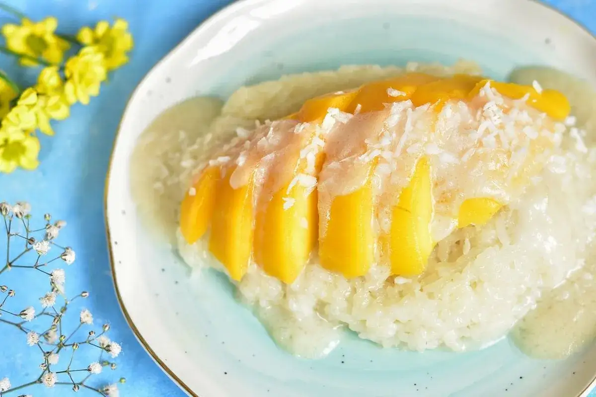 Pyszny deser mango sticky rice przepis: kleisty ryż z mlekiem kokosowym, polany sosem i posypany wiórkami kokosowymi, z kawałkami mango na wierzchu.