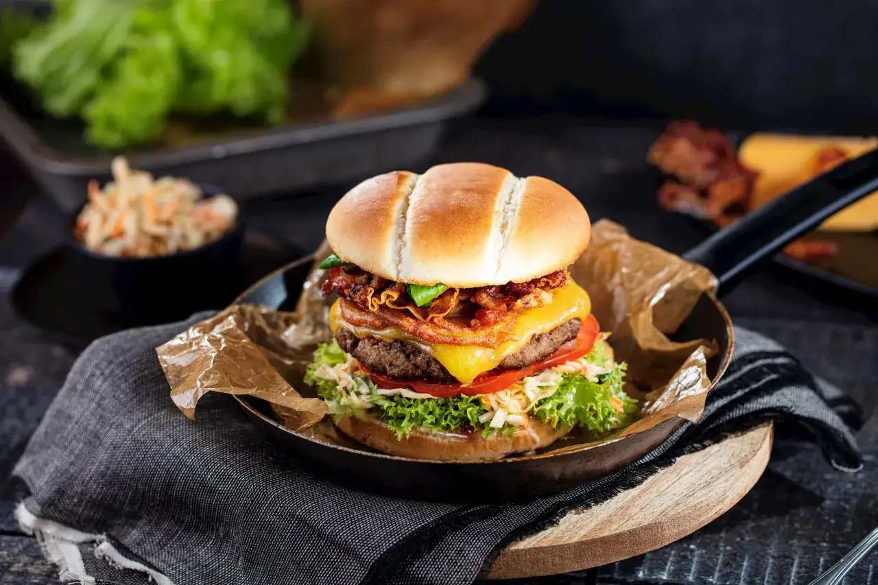 Apetyczny burger z chrupiącym boczkiem, serem i świeżymi warzywami. Idealny dodatek do burgera to surówka z kapusty i marchewki.