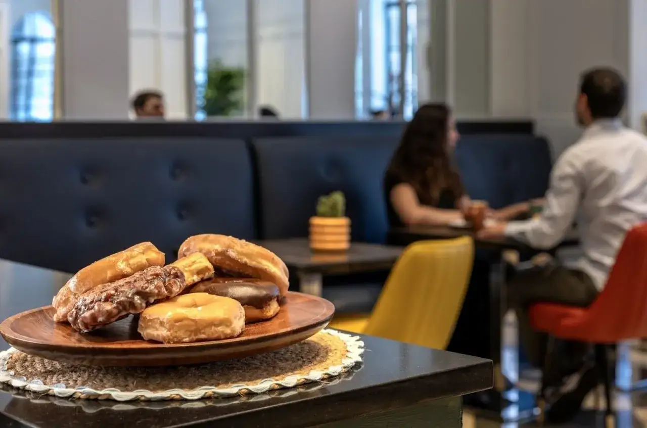 Pyszne pączki na talerzu w hotelowym lobby. Para siedzi przy stoliku w tle, delektując się chwilą.