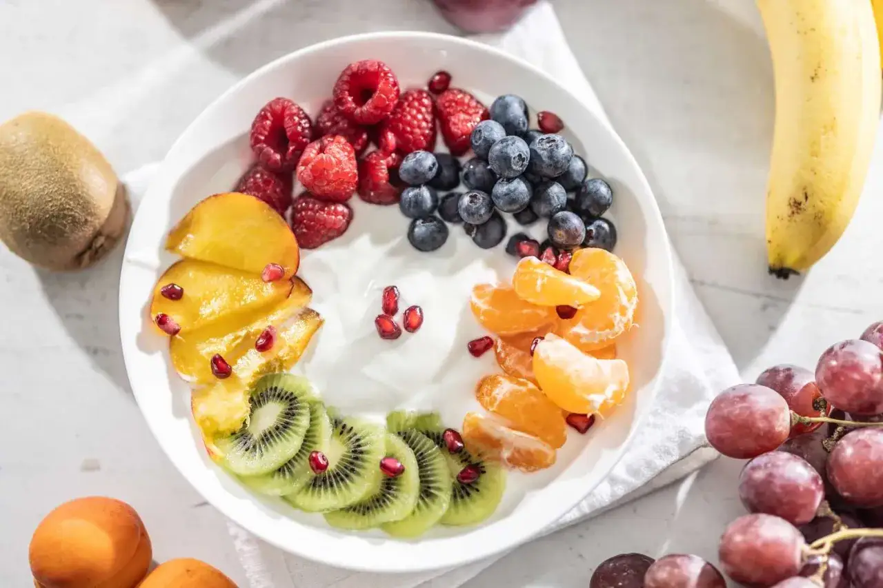 Kolorowy jogurt z owocami: maliny, borówki, brzoskwinie, kiwi, mandarynki i granat. Idealne co zamiast chleba na śniadanie.
