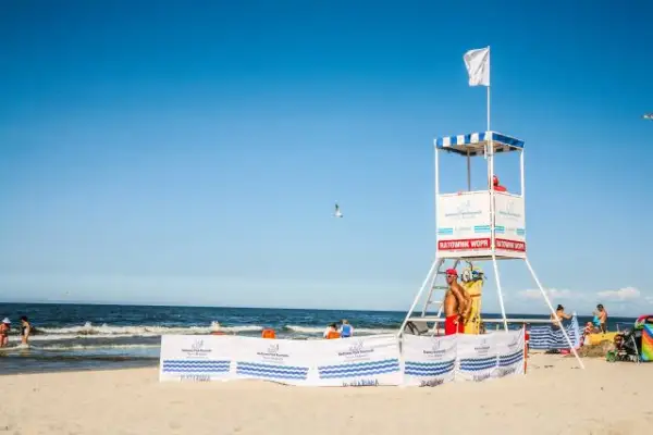 Biała flaga nad morzem oznacza bezpieczną kąpiel. Ratownik czuwa z wieży ratowniczej na plaży.