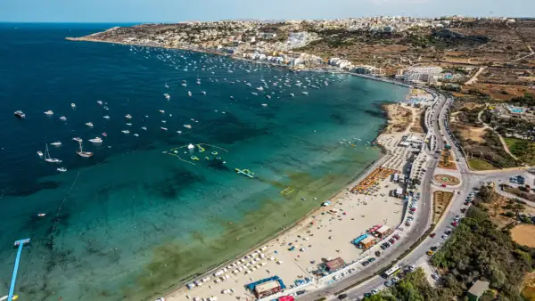 Malta zachwyca turkusowym morzem pełnym łodzi i wodnych atrakcji. Plaże tętnią życiem, a miasto rozciąga się wzdłuż wybrzeża.
