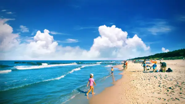Słoneczna plaża, fale, dzieci bawiące się w piasku i w wodzie. W tle widać las i ludzi cieszących się wakacjami. Idealne miejsce na chałupy imprezy.
