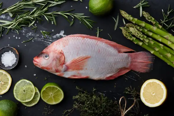 Cała ryba tilapia, świeże szparagi, cytryny, limonki, rozmaryn i sól morska na czarnym tle. Tilapia co to za ryba?