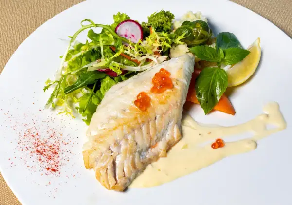 Filet morszczuka z ikrą, podany z sałatką, warzywami i sosem. Czy morszczuk jest zdrowy? Tak, to chuda ryba bogata w białko.