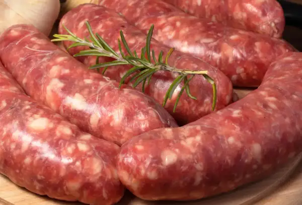 Świeża, surowa kiełbasa włoska z gałązką rozmarynu i czosnkiem w tle.