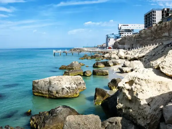 Brzeg największego morza w Europie, z turkusową wodą, kamienistą plażą i nowoczesnymi budynkami na klifie.