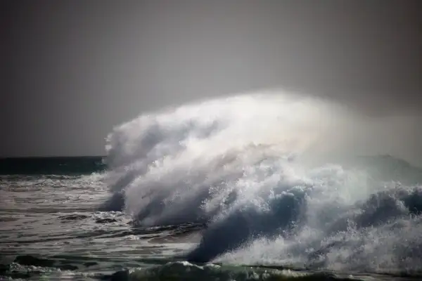 Potężna fala rozbija się na tle burzowego nieba. Woda w **oceanie atlantyckim** jest wzburzona, tworząc kaskady piany i bryzgów.