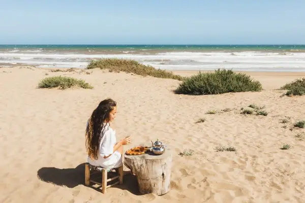 Kobieta pije herbatę na piaszczystej plaży. W tle widać turkusowe morze, które przypomina o pięknie Tunezji.