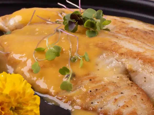 Smażony filet rybny w sosie, udekorowany kiełkami i żółtym kwiatem. Czy amur ma dużo ości? Ten wygląda na bezproblemowy.