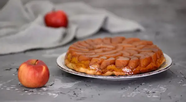 Apetyczna tarta tatin przepis na pyszny deser z karmelizowanymi jabłkami. Obok leży świeże jabłko.