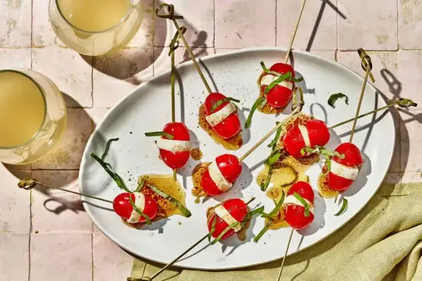Kolorowe szaszłyki z pomidorkami koktajlowymi i mozzarellą, polane sosem. Idealne zdrowe przekąski na przyjęcie.