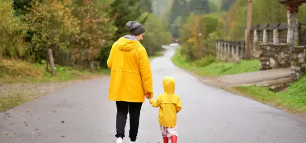 Mama i dziecko w żółtych płaszczach idą za rękę mokrą drogą. Nawet w deszczowe dni Jastarnia oferuje atrakcje, jak spacery po malowniczych okolicach.