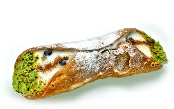 Sycylijskie dania: chrupiąca rurka cannoli z kremem, pistacjami i borówkami, posypana cukrem pudrem.