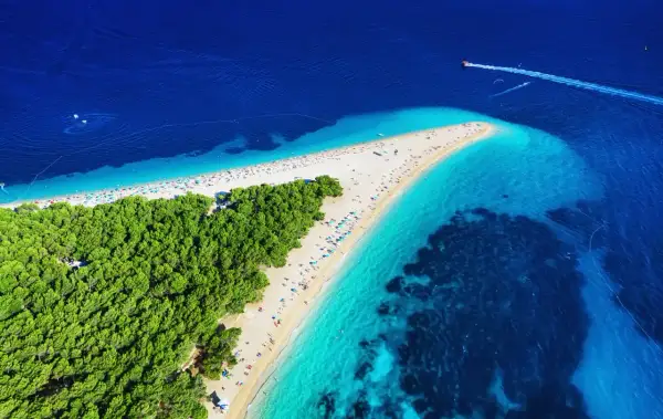 Widok z lotu ptaka na plażę w Chorwacji, gdzie turkusowe morze spotyka się z zielonym lasem sosnowym. Idealne miejsce na wakacje.