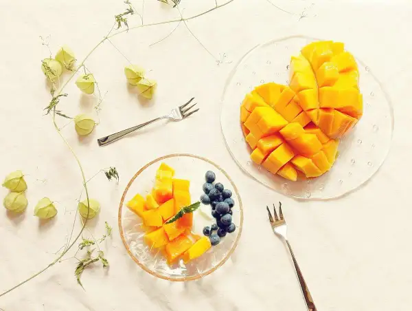 Słodkie mango pokrojone w kostkę, idealne do jedzenia z jagodami i jogurtem. Obok gałązka z zielonymi pąkami.