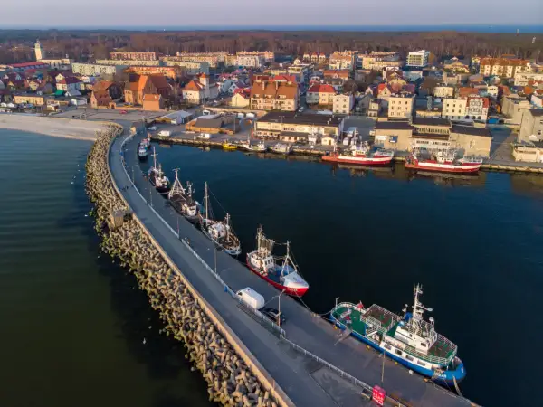 Port w Helu poza sezonem. Spokojne wody, zacumowane kutry i statki, a w tle miasto i las.