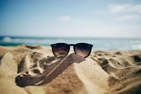 Okulary przeciwsłoneczne na piaszczystej plaży, w tle morze i błękitne niebo. Idealne na wakacje, gdy obowiązuje opłata klimatyczna nad morzem.
