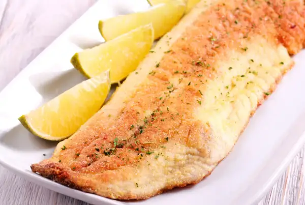 Smażony filet z ryby amur, podany z ćwiartkami limonki. Delikatny smak amura świetnie komponuje się z cytrusową nutą.